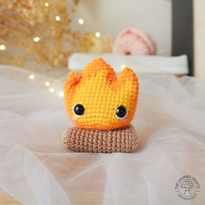 May include: A crocheted amigurumi doll of a campfire with a yellow and orange flame and a brown log base. The doll has black eyes and a pink blush.