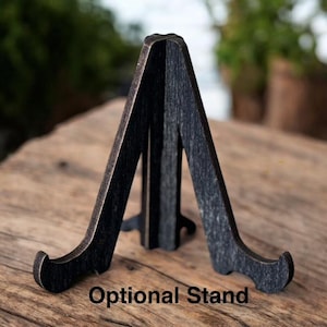 May include: A dark-stained wooden easel stand with an A-frame design. The stand has a curved base and is designed to hold a picture or other display item. The text "Optional Stand" is printed at the bottom.