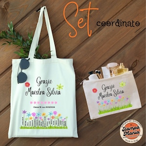 Può includere: Un set di due borse in tela bianca con disegni floreali e il testo "Grazie Maestra Silvia". La borsa più grande è una borsa a tracolla con manico e la borsa più piccola è una pochette con cerniera. La borsa a tracolla ha il testo "Classe 1B a.s. 2023/2024" e una fila di fiori con nomi sotto.