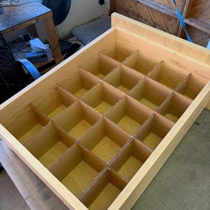 May include: A wooden box with a grid of compartments, perfect for organizing small items. The box is made of light wood and has a natural finish.