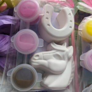Puede incluir: Un kit de manualidades en una bolsa de pl&aacute;stico transparente que contiene una herradura de yeso blanco y una figura de cabeza de caballo de yeso blanco. El kit incluye tres peque&ntilde;os botes de pintura redondos con pintura rosa y marr&oacute;n.