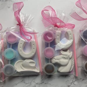 Puede incluir: Cuatro bolsas de pl&aacute;stico transparente con figuras de yeso blanco de caballos, botas de vaquero, sombreros de vaquero y herraduras. Cada bolsa incluye peque&ntilde;os recipientes circulares de pintura, un pincel fino y un lazo rosa.