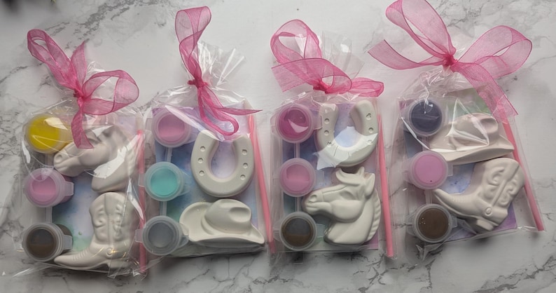 Puede incluir: Cuatro bolsas de pl&aacute;stico transparente con figuras de yeso blanco de caballos, botas de vaquero, sombreros de vaquero y herraduras. Cada bolsa incluye peque&ntilde;os recipientes circulares de pintura, un pincel fino y un lazo rosa.