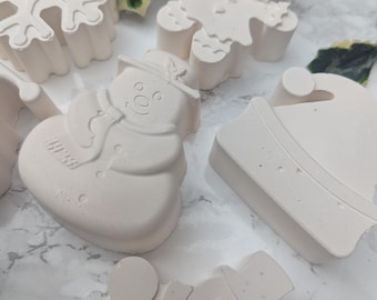 Könnte beinhalten: Eine Sammlung cremefarbener Weihnachtsornamente. Die Ornamente umfassen eine Schneeflocke, einen Lebkuchenmann, einen Schneemann, einen Weihnachtsmannhut und andere Schneemannformen. Die Ornamente sind auf einer hellen Oberfläche angeordnet.