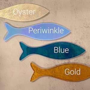 May include: Four fish-shaped decorative items in shades of oyster, periwinkle, blue, and gold. Each fish has a different color and the name of the color is written on each fish. The fish are arranged on a neutral background.