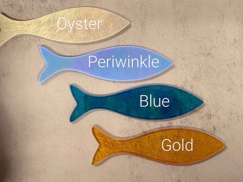 May include: Four fish-shaped decorative items in shades of oyster, periwinkle, blue, and gold. Each fish has a different color and the name of the color is written on each fish. The fish are arranged on a neutral background.