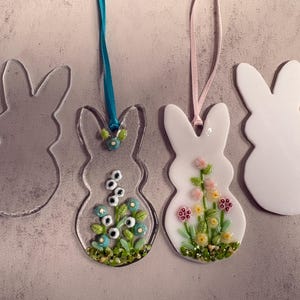 May include: Bunny-shaped ornaments. Two clear glass bunnies and two white bunnies. One clear bunny has blue and white floral accents. The other white bunny has pink and yellow floral accents. Each has a ribbon for hanging.