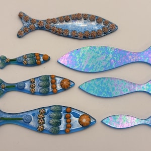 May include: A collection of decorative fish in various sizes and designs. Some fish are blue with orange and green accents, while others have an iridescent, opalescent finish. These handcrafted fish are suitable for home decor.