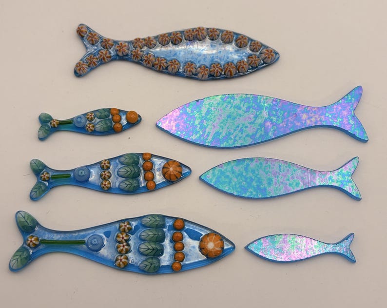 May include: A collection of decorative fish in various sizes and designs. Some fish are blue with orange and green accents, while others have an iridescent, opalescent finish. These handcrafted fish are suitable for home decor.