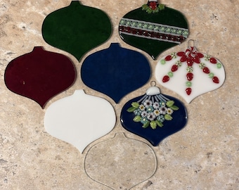 May include: A collection of seven teardrop-shaped glass ornaments in various styles. The set includes solid dark green, deep red, navy blue, and white pieces, alongside three decorated ornaments featuring floral, striped, and peppermint-like patterns.