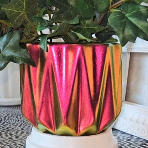May include: A red and green iridescent ceramic planter with a geometric design. The planter is filled with green ivy.