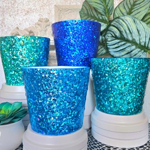 May include: Four glitter-covered ceramic pots in shades of blue and green. The pots are all different sizes and have a sparkly finish.