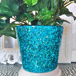 May include: A turquoise glitter planter with a green ivy plant growing out of it. The planter is sitting on a white base.