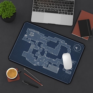 May include: A rectangular mouse mat featuring a blue and white blueprint design. A white computer mouse rests on the mat. A laptop, notebooks, pencils, and a coffee cup are also visible.