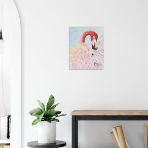 Op de afbeelding: Schilderij van een roze flamingo met een rode snavel en nek, tegen een lichtblauwe achtergrond. Het kunstwerk bevat het woord "Pink". De veren van de flamingo zijn afgebeeld in roze tinten.
