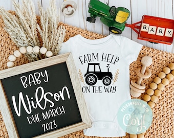 May include: A white onesie with the text "Farm Help On The Way" and a black silhouette of a tractor. A wooden sign with the text "Baby Wilson Due March 2023" is in the background.