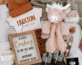 May include: A baby announcement featuring a brown beanie, a onesie with "Huxton James" printed on it, a stuffed animal, a framed sign that reads "A Little Cowboy is on the Way Arriving October 2026", and baby cowboy boots.