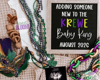 May include: A white baby onesie, Mardi Gras beads, a letter board with text, a baby ultrasound, and a wooden toy are arranged on a neutral-toned blanket. The letter board reads "Adding Someone New to the Krewe Baby King August 2026."