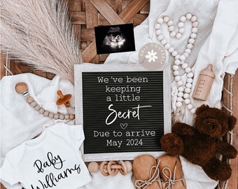 May include: A gender reveal announcement with a black letter board that reads "We've been keeping a little secret. Due to arrive May 2024". The board is surrounded by a white blanket, a baby onesie, a wooden rattle, a teddy bear, a wooden bottle, and a small wooden bead garland.