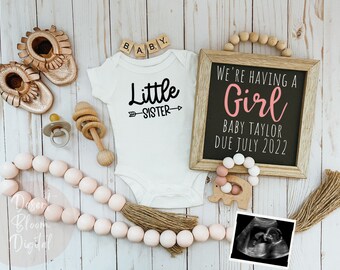 Könnte beinhalten: Eine Geschlechter-Enthüllungsanzeige mit einem weißen Strampler, auf dem "Kleine Schwester" steht, und einem schwarzen Schild, auf dem "Wir bekommen ein Mädchen Baby Taylor Erwartet im Juli 2022" steht.