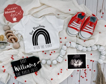 May include: A white onesie with a black rainbow and the text "Our Rainbow After The Storm". A wooden rattle, a pair of red baby shoes, a black sign with the text "Baby Williams Due March 2022", a white beaded garland, and a black and white ultrasound image are also in the image.