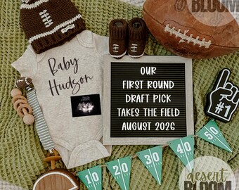 May include: A football-themed baby announcement with a brown and white knit hat, matching booties, and a onesie that says "Baby Hudson." Includes a football, a letter board, and a banner with yard markers.
