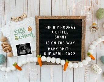 Peut inclure: Un body blanc avec le texte "egg-cited" et un motif d'œuf vert et orange. Un tableau d'affichage avec le texte "Hip Hip Hooray A Little Bunny Is On The Way Baby Smith Due April 2022". Une guirlande blanche et orange avec des carottes et des pompons blancs. Un fond en bois blanc.