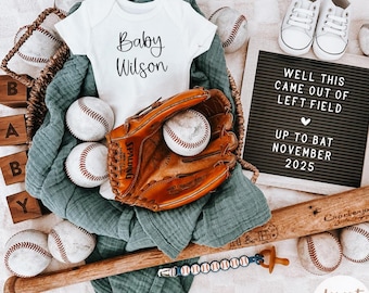 May include: A baby announcement featuring a white onesie with "Baby Wilson" in script, baseballs, a brown leather glove, a wooden baseball bat, and a letter board that reads "Well this came out of left field, up to bat November 2025".