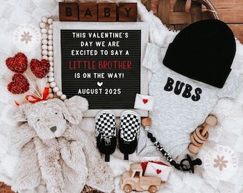 May include: A black letter board with the text "This Valentine's Day We Are Excited To Say A Little Brother Is On The Way! August 2025".  A gray onesie with the text "BUBS" in black.  A pair of black and white checkered baby shoes.  A wooden toy truck.  A stuffed animal.  A wooden rattle.  A black and white beaded pacifier clip.  Red and white heart decorations.