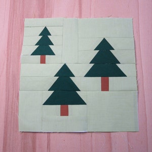 Könnte beinhalten: Eine grüne Stoff-Patchwork-Decke mit drei grünen Weihnachtsbäumen mit braunen Stämmen. Die Decke liegt auf einer hellrosa Holzoberfläche.