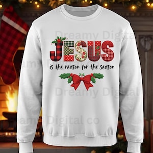 May include: White crew neck sweatshirt with the text "JESUS is the reason for the season". The word "JESUS" is in a plaid and floral design. A red bow and holly leaves are at the bottom of the design.