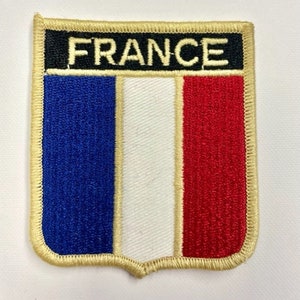 May include: A blue, white, and red embroidered patch with the word "FRANCE" in black lettering on a gold background.