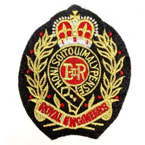 Puede incluir: Parche bordado negro con detalles dorados y rojos. El diseño incluye una corona, ramas de laurel y el texto "ROYAL ENGINEERS". Un círculo rojo en el centro muestra "ER" y texto adicional.