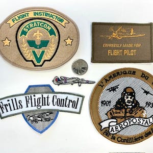 May include: A selection of vintage flight patches. One patch reads "Flight Instructor Stratcom" with a green and gold design. Another says "Expressly Made For Flight Pilot." A third patch says "Frills Flight Control."