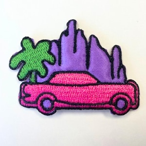May include: Embroidered iron-on patch featuring a pink car with a green palm tree in front of a purple mountain range.