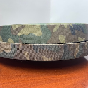 May include: Two rolls of camouflage patterned webbing. The webbing is a dark green, brown, and tan color.