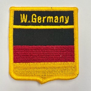 Puede incluir: Un parche bordado amarillo, negro y rojo con el texto "W. Germany" en hilo amarillo.