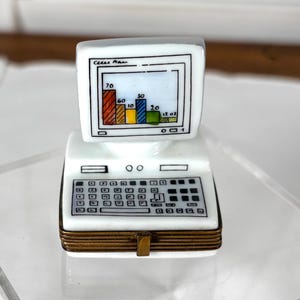 Peut inclure: Un ordinateur miniature blanc avec un clavier et un écran affichant un graphique à barres. L'écran montre un tableau coloré avec des barres rouges, jaunes, bleues et vertes. L'ordinateur est posé sur une surface en acrylique transparente.