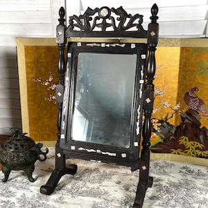 Peut inclure: Un miroir de toilette vintage en bois avec une finition noire et des sculptures complexes. Le miroir a un cadre rectangulaire avec un bord biseauté et est décoré d'accents en nacre. Le miroir est sur un pied à trois pieds.