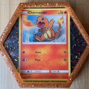 Puede incluir: Una carta de juego de Pokemon con Charmander, un Pokemon de tipo fuego. La carta está en un marco hexagonal con un fondo de purpurina negro y rojo. La carta tiene un esquema de color rojo, naranja y amarillo. El texto de la carta dice "BASIC Charmander HP70 NO. 004 Lizard Pokemon HT 2'00" WT 18.7 lbs. Gnaw 10 Flare 20 weakness x2 resistance retreat The flame on its tail indicates Charmander's life force. If it is healthy, the flame burns brightly."