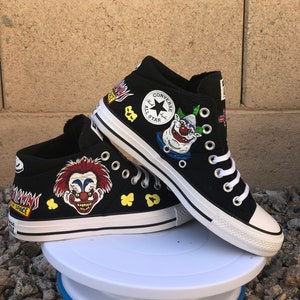 May include: Black Converse high-top trainers with custom painted designs. The shoes feature a clown face, popcorn, and the words "Space Clown".