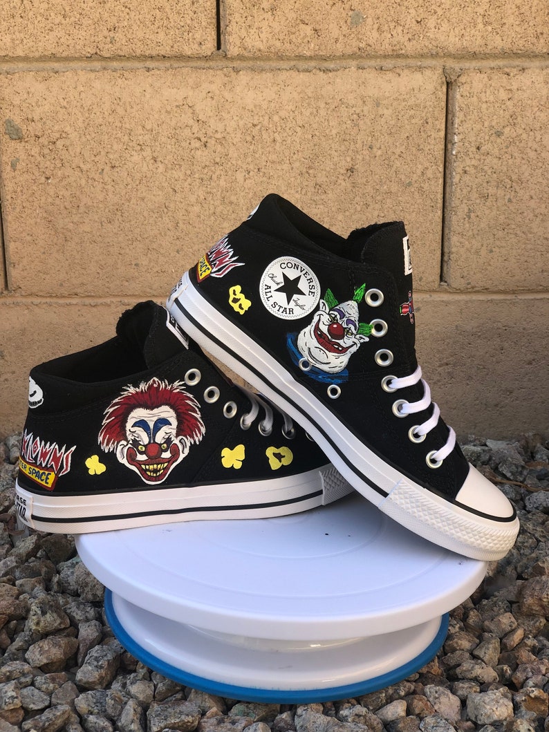 May include: Black Converse high-top trainers with custom painted designs. The shoes feature a clown face, popcorn, and the words "Space Clown".
