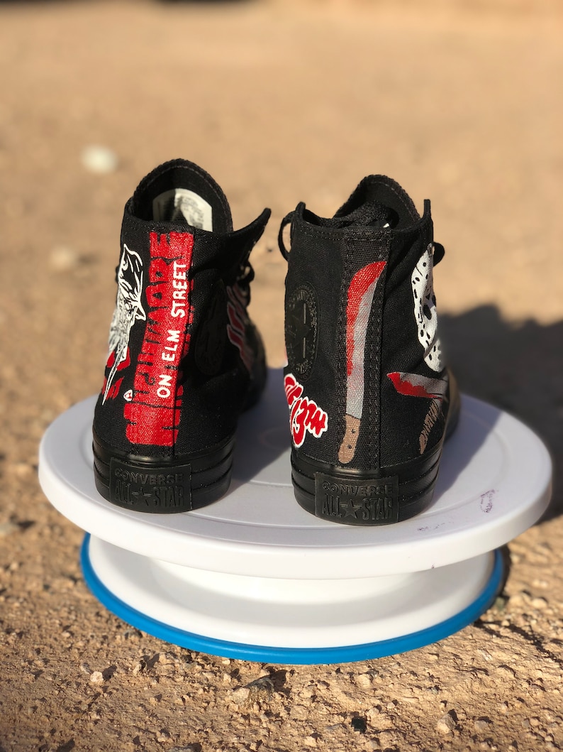 May include: A pair of black high-top Converse sneakers with a custom design featuring a white and red Freddy Krueger character from the movie "A Nightmare on Elm Street". The sneakers have the text "A Nightmare On Elm Street" on the side.