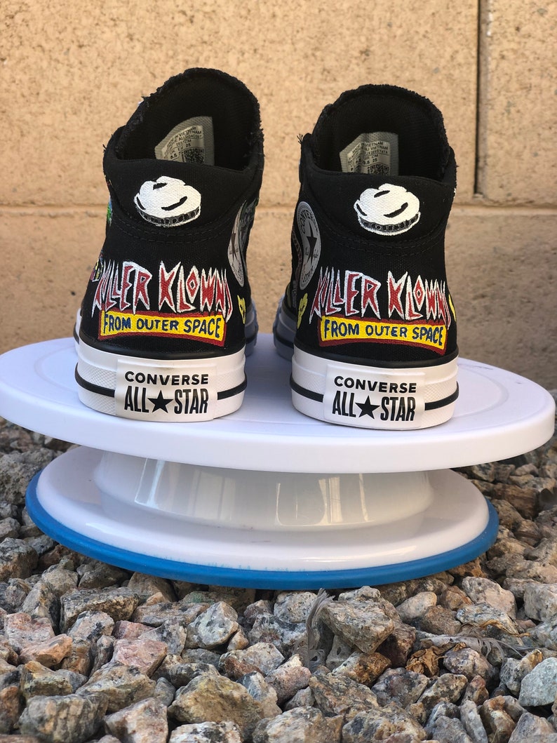 May include: A pair of black high-top Converse sneakers with custom painted designs. The sneakers feature a graphic of a clown with the text "Killer Klowns from Outer Space".