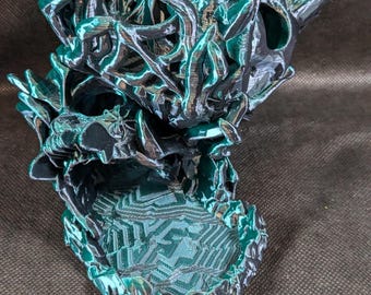 Może przedstawiać: Teal i czarna dekoracyjna rzeźba czaszki z geometryczną podstawą. Czaszka ma ostre, krystaliczne wypustki i metaliczny połysk. Rzeźba jest ustawiona na ciemnym tle.