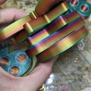 May include: A stack of iridescent rainbow-coloured silicone fidget toys in the shape of a butterfly. The toys are made of a soft, flexible material and have a smooth, glossy finish.