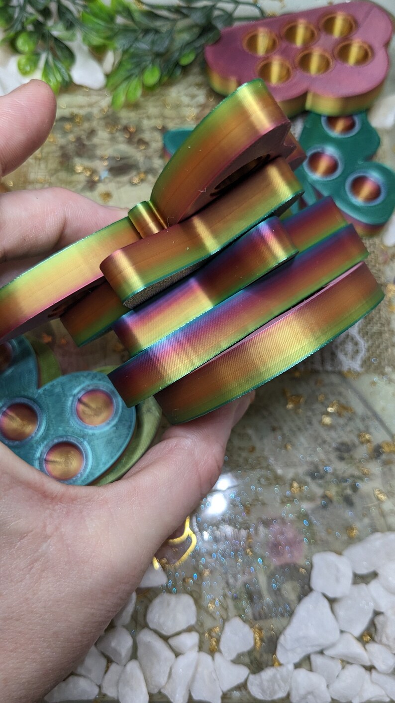 May include: A stack of iridescent rainbow-coloured silicone fidget toys in the shape of a butterfly. The toys are made of a soft, flexible material and have a smooth, glossy finish.