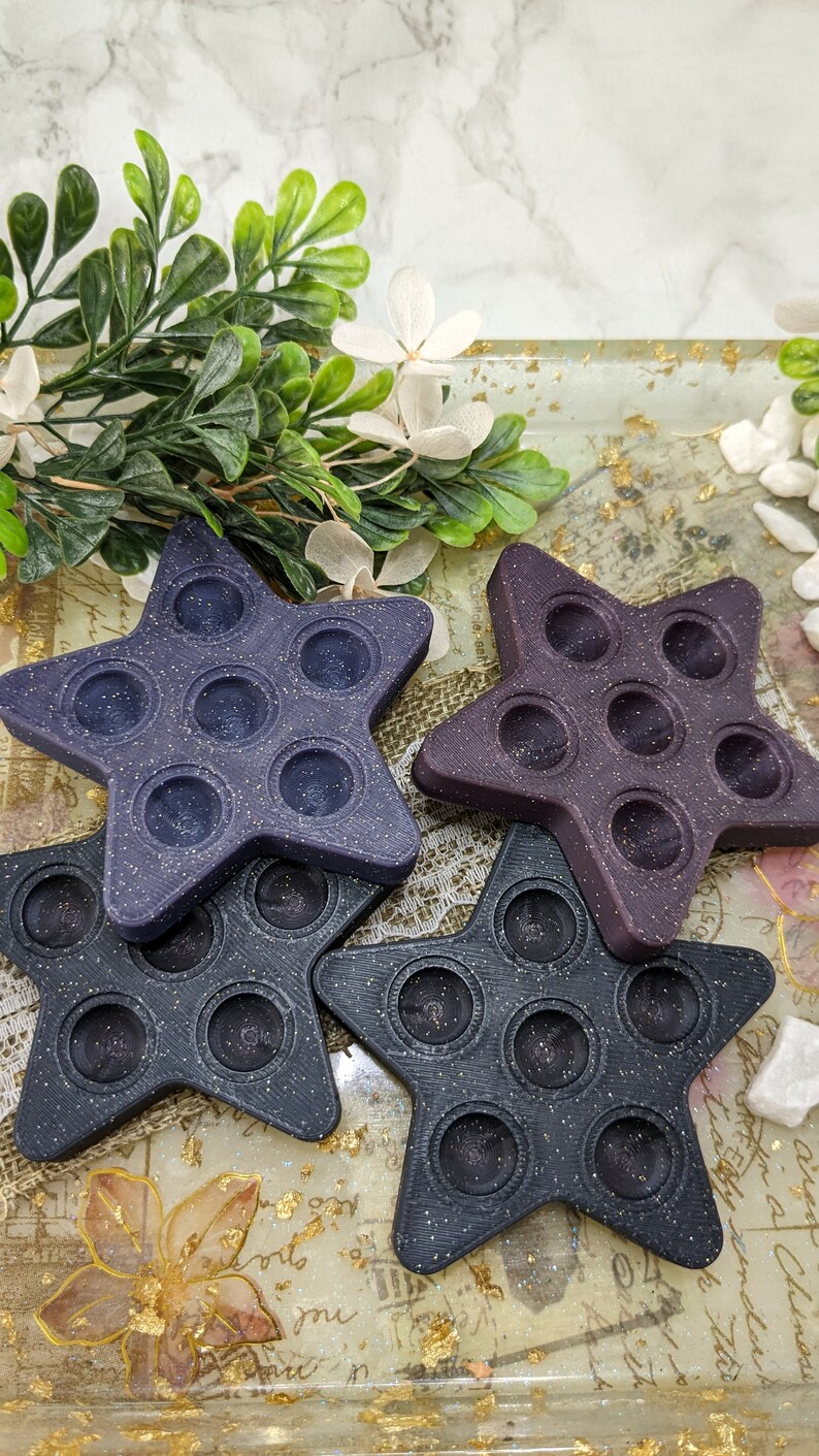 May include: Three star-shaped pop-it fidget toys in different shades of purple and black. The toys are made of silicone and have a textured surface.