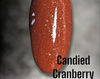 Może przedstawiać: Zbliżenie na mały słoiczek czerwonego lakieru do paznokci z brokatem z napisem "Bloom Dip" i "Candied Cranberry" na etykiecie.