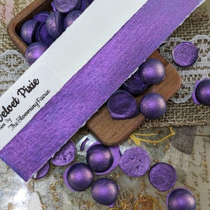May include: A sample of purple iridescent paint called "Velvet Pixie" by The Blooming Faerie. The paint is shown on a white card with a purple iridescent sheen. The paint is also shown in small round beads.